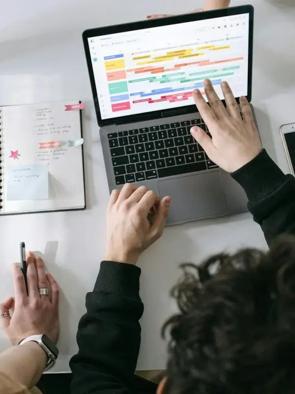 Two people collaborating on a laptop and planner at a vibrant modern office desk.