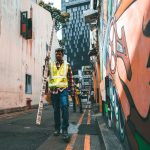 A construction worker walks down a vibrant alley in Singapore, highlighting the city's unique urban art scene.